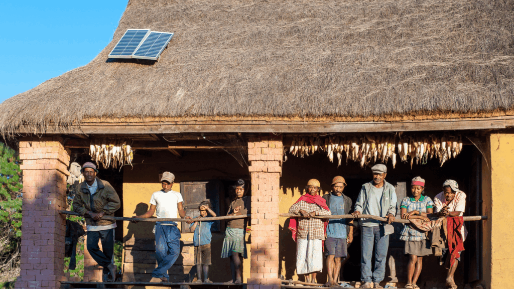 A rural home electrified by solar technology through Barefoot College International's Solar training programme. A family stand in the porch of their home, with a solar panel on the roof.