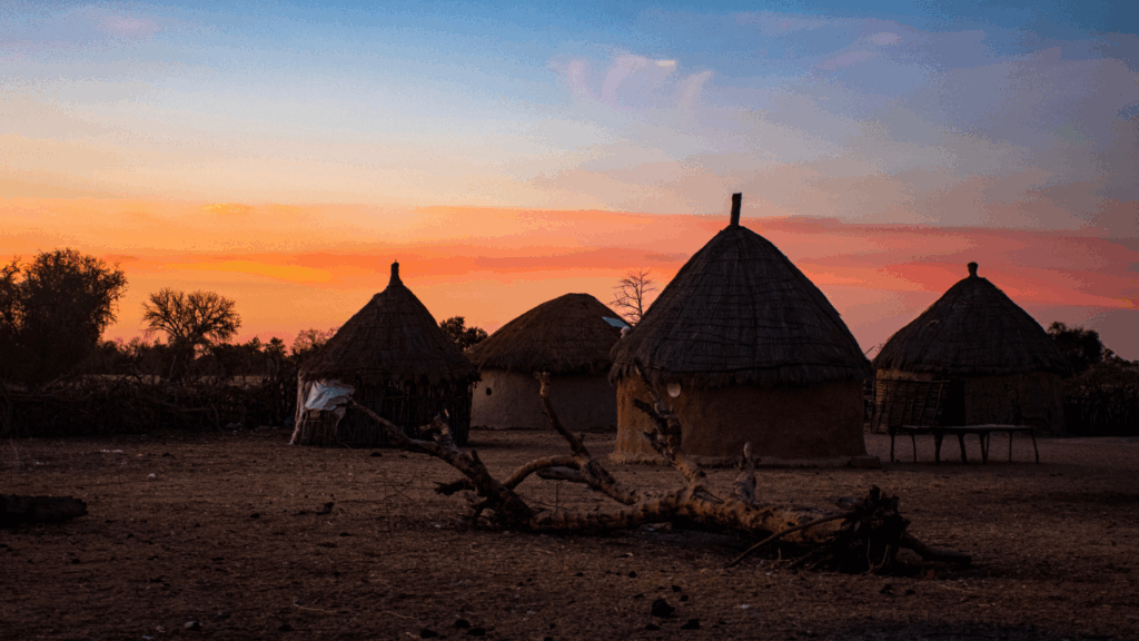 Three rural homes in a village in Senegal with a sunset behind them. You can see that the homes have been electrified with solar energy by the solar engineers from Barefoot College International